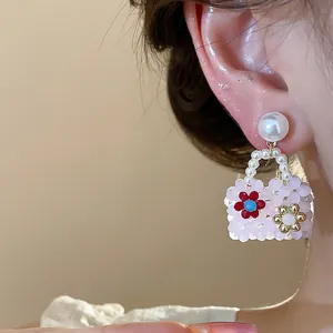 Close-up of a pink beaded handbag-shaped earring with flower details and a white pearl stud.