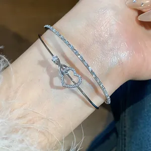Detalle de cerca de un brazalete de doble capa plateado con corazón de pavé y nudo infinito