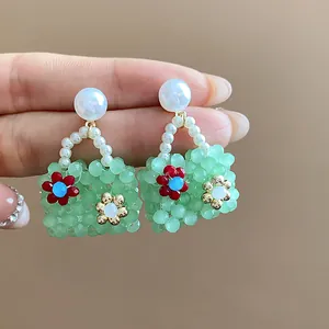 Close-up of green beaded handbag earrings with pearl studs and floral accents.
