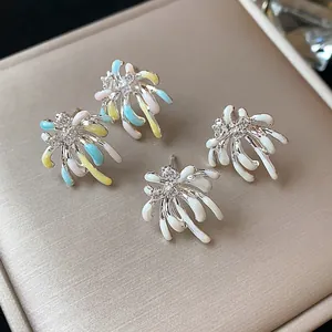 Close-up of firework-inspired stud earrings with colorful enamel and sparkling zircons on a pad