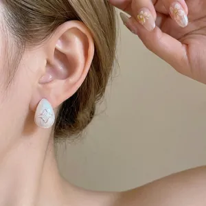 Elegant white teardrop earrings with sparkling star cutout design on model's ear.