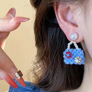 Handcrafted blue beaded handbag earring with pearl stud and flower detail close-up.