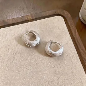 Minimalist textured silver hoop earrings with zircon star accents on beige background