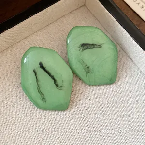 Dettaglio di orecchini a lobo in resina verde con motivo marmorizzato a inchiostro.