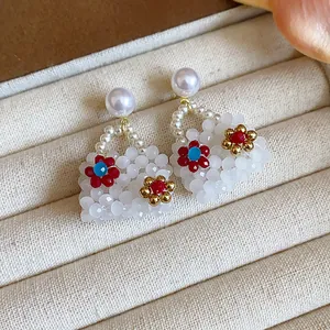 Macro view of handmade handbag-shaped pearl earrings with colorful flower bead accents.