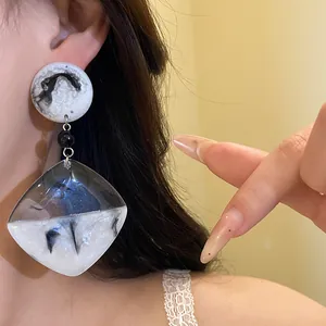 Primo piano di orecchini pendenti in resina marmorizzata con aghi in argento su modella.