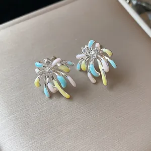 Close-up of colorful enamel firework stud earrings with zircon details on beige box.