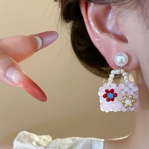 Close-up of pink beaded handbag earrings with pearl stud and flower detail.