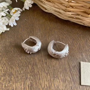 Close-up of minimalist silver hoop earrings with zircon starburst texture on wood background