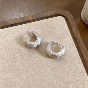 Detailed macro view of textured silver huggie hoop earrings featuring tiny zircon star accents