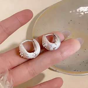 Close-up of textured silver hoop earrings with small starburst motif.
