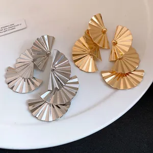 Macro detail of stylish pleated fan-shaped drop earrings in gold and silver metal.