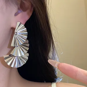 Close-up detail of silver triple-layered pleated fan drop earrings on model