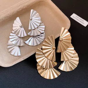 Macro view showing gold and silver pleated fan-shaped dangle earrings with metallic texture