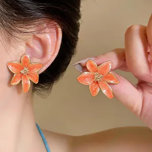 Vista dettagliata di eleganti orecchini a fiore color pesca con finitura dorata di lusso