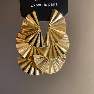Layered gold pleated fan-shaped pendant earrings displayed on a black cardboard tag