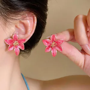 Dettaglio ravvicinato di eleganti orecchini a fiore rosa con bordi dorati su modella