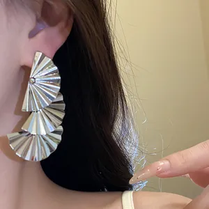 Close-up of silver-toned pleated fan-shaped pendant earrings worn on a model's ear