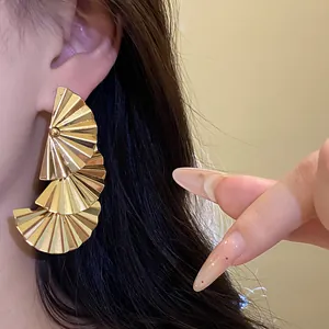 Close-up detail of elegant gold tiered fan-shaped pleated drop earrings worn on model's ear