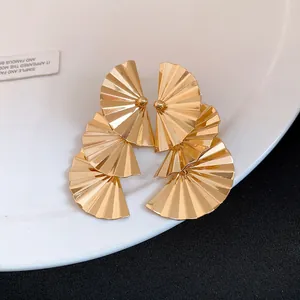 Elegant golden tiered fan-shaped earrings with a metallic pleated finish on a white plate