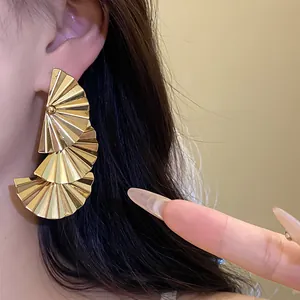Close-up detail of stylish layered gold pleated fan-shaped earrings on a female ear