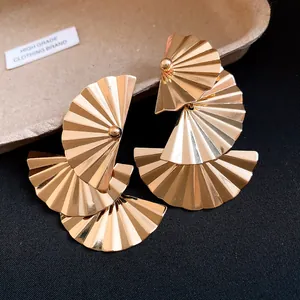 Close-up of gold tiered fan earrings showing metallic pleats and high-shine finish.