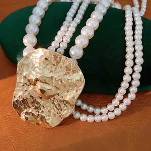 Multi-strand pearl necklace featuring a large hammered gold-tone statement pendant.