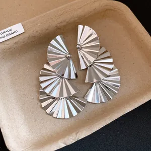 Macro detail view of elegant silver-toned pleated fan-shaped metal pendant earrings