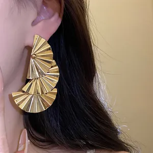 Close-up macro view of stylish golden multi-tiered pleated fan-shaped pendant earrings on ear