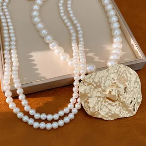 Close-up detail of double-layer pearl necklace with large gold hammered pendant.