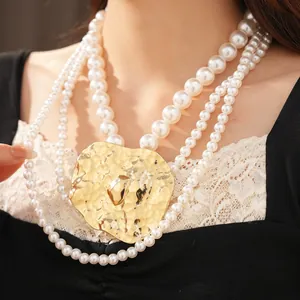 Detailed view of multilayer pearl necklace with a large hammered gold pendant.