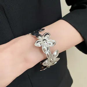Detailaufnahme eines silberfarbenen offenen Metall-Blumenarmbands am Handgelenk eines Models