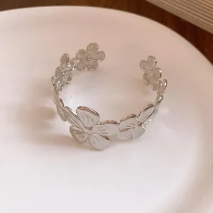 Detailansicht eines eleganten silbernen Blumen-Armreifs auf einem Keramikteller.