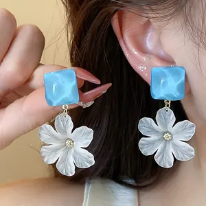 Dettaglio ravvicinato di eleganti orecchini quadrati blu e fiori di acrilico bianchi
