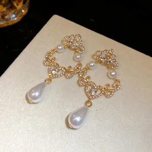 Detail of vintage gold earrings with heart-shaped scrollwork, crystals, and teardrop pearls.