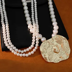 Detailed view of the hammered gold pendant on a multi-strand white pearl necklace jewelry