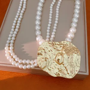Close-up detail of multi-strand pearl necklace featuring a large hammered gold metal pendant