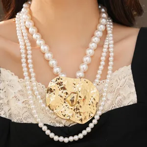 Close-up of multi-strand pearl necklace with oversized hammered gold metal pendant