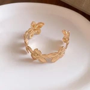 Detailaufnahme eines eleganten goldfarbenen Blumen-Armreifs auf einem weißen Keramikteller