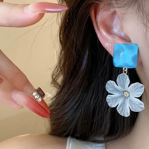 Primo piano di un orecchino a fiore bianco con quadrato in acrilico blu indossato all'orecchio