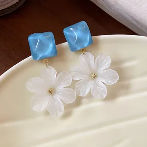 Dettaglio di orecchini a fiore in acrilico bianco con perni quadrati azzurri su piatto
