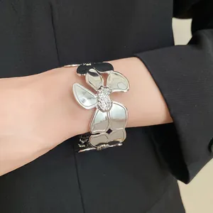 Nahaufnahme eines großen silbernen Metall-Blumenarmreifs mit strukturierter Mitte am Handgelenk.
