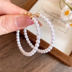 Close-up of elegant pearl hoop earrings with gold-toned posts on retro background.