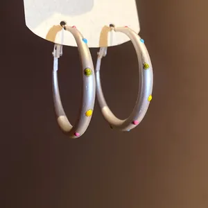 Detailed close-up showing matte silver hoop earrings adorned with vibrant colorful enamel dots