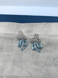 Detailed close-up of elegant fog blue ribbon bow earrings with sparkling rhinestone floral accents