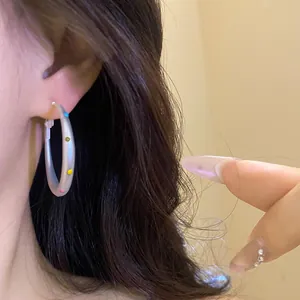Close-up detail of frosted white hoop earrings with colorful polka dots worn on ear