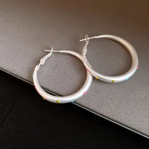 Close-up view of matte silver hoop earrings featuring vibrant colorful polka dot accents