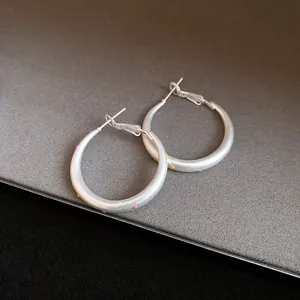 Detail view of minimalist matte silver hoop earrings with vibrant colored polka dot accents