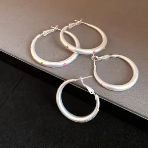 Close-up detail of minimalist matte silver hoop earrings with colorful polka dots
