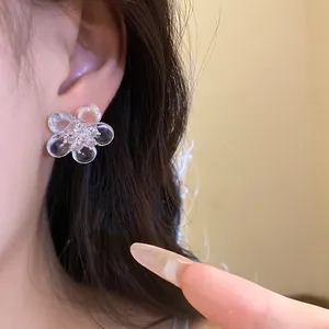 Close-up view of a delicate clear resin flower stud earring with sparkling stones worn on ear